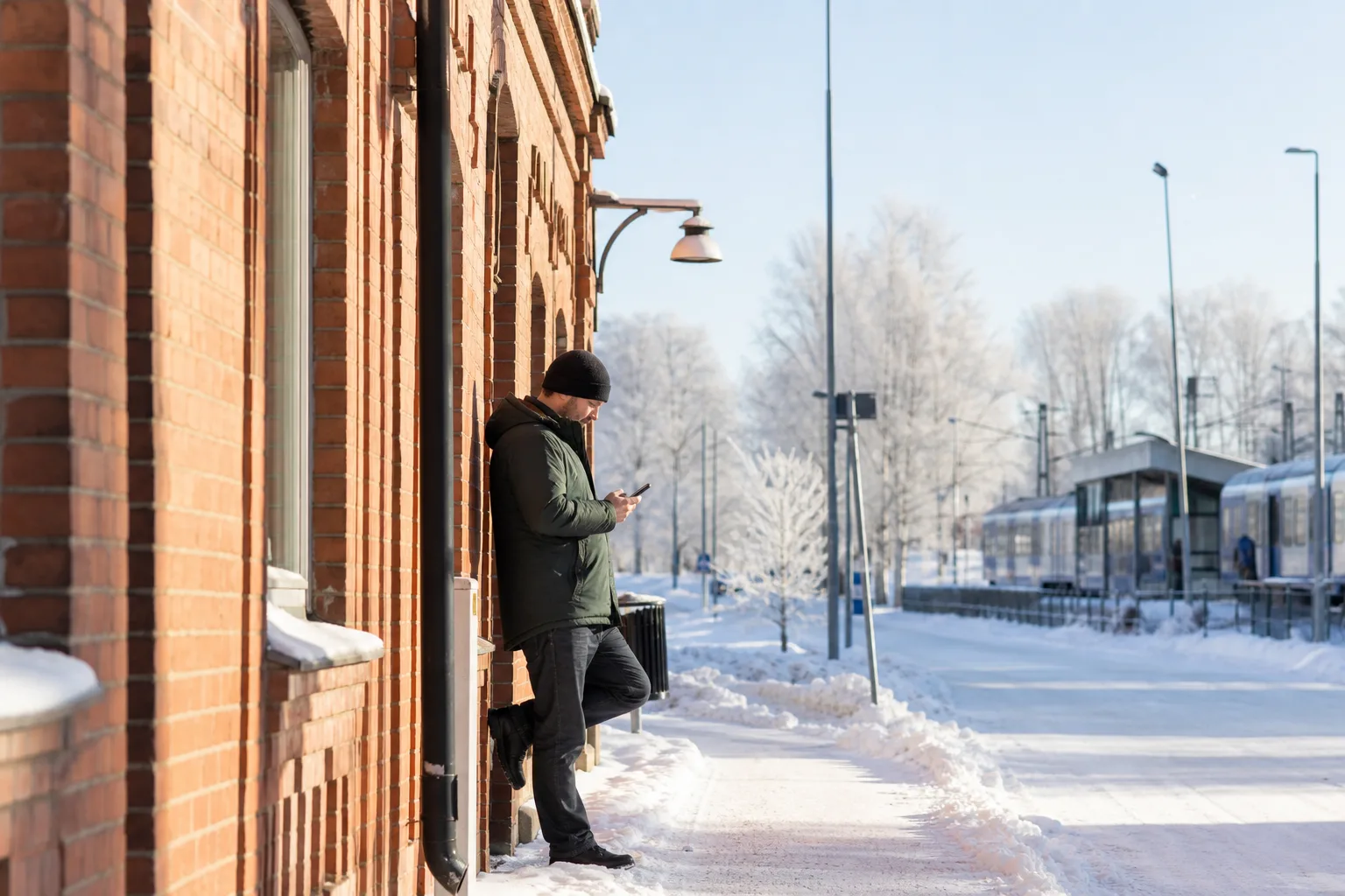Person med mobil vid en äldre tegelbyggnad på en snötäckt gata i garnisons- och järnvägsstaden Boden en klar vintermorgon