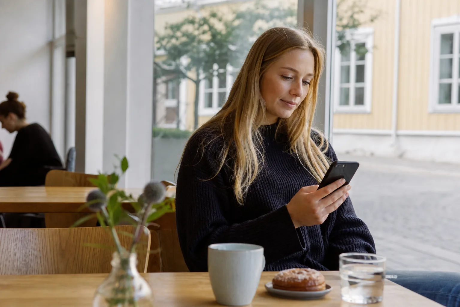 En person tittar på sin dataanvändning i mobilen vid ett café-bord i en vardaglig nordisk miljö i dagsljus.