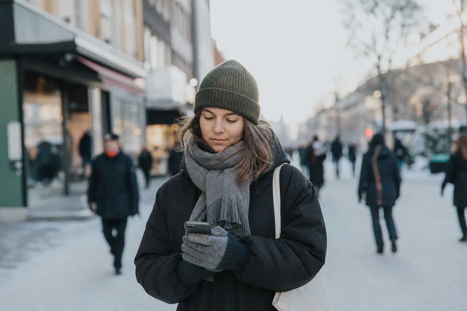 Ung person på en gågata i en nordsvensk vinterstad med Umeå-känsla tittar på sin mobil – Tres nät är snabbast i städerna i norr.